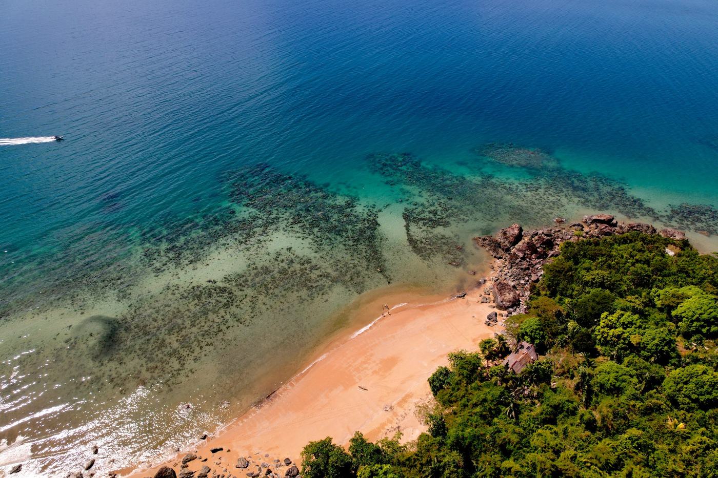 Un bateau traverse le lagon le long de la côte, entre récifs et plage